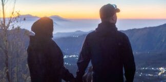 A couple holding hands while enjoying a beautiful sunrise over the misty caldera, highlighting the romantic and unforgettable experience of a Mount Bromo tour package